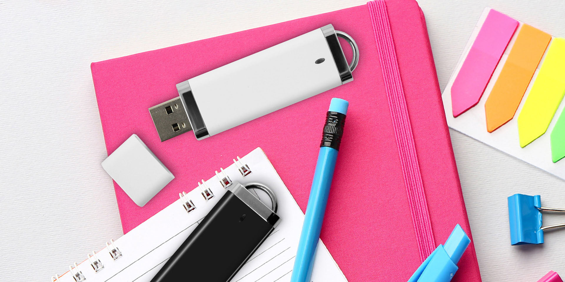 USB UBU marki Goodram leżące na notatnikach razem z artykułami biurowymi